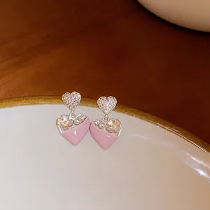 Close-up of pink heart-shaped earrings with rhinestones and flower details.
