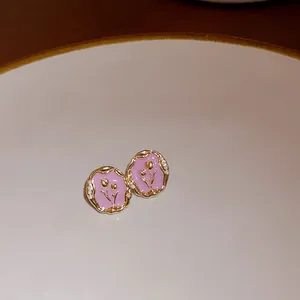 Close-up of pink enamel floral stud earrings with gold-toned pearl-trimmed borders.