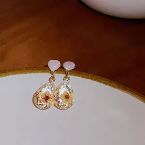 Detailed macro view of pink heart stud earrings with yellow dried flower teardrop pendants