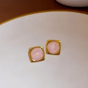 Detail view of square pink gemstone stud earrings with a polished gold-tone frame.