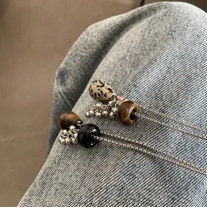 Close-up detail of natural tiger's eye and dalmatian stone teardrop pendants on silver chain.
