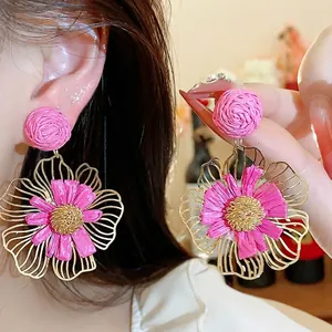 Große rosa Raffia-Blumenohrringe mit goldfarbenen Metallblüten und Silbernadeln.