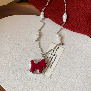 Detailed view of a red flocked rocking horse pendant on an elegant pearl necklace chain