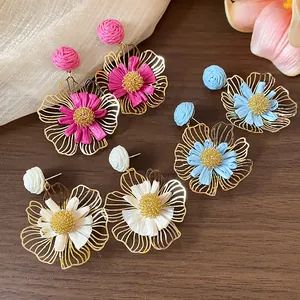 Detailansicht von handgefertigten Raffia-Blumenohrringen in drei Farben auf Holz