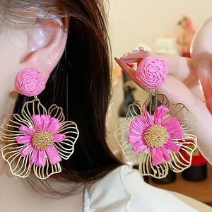Detailaufnahme der handgefertigten rosa Raffia-Blumenohrringe mit Goldmetallrahmen