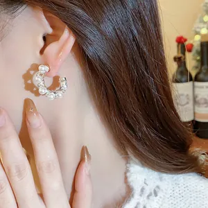 Detailed view of an elegant C-shaped hoop earring with pearls and zircon on a model's ear