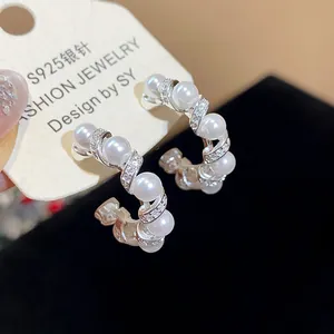 Close-up detail of elegant C-shaped pearl earrings featuring sparkling pavé zircons