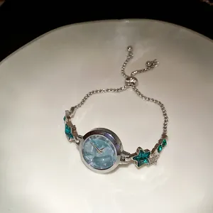 Close-up of elegant silver star bracelet watch with light blue dial and green stones