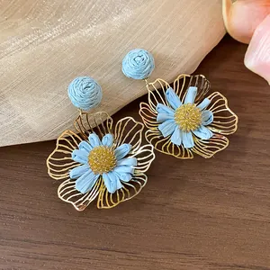 Nahaufnahme hellblauer Bast- und goldfarbener Metall-Blumenohrringe Designdetails