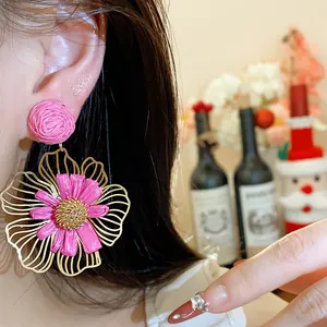 Nahaufnahme von rosa Raffia-Blumenohrringen mit goldenem Metallrahmen für den Urlaub