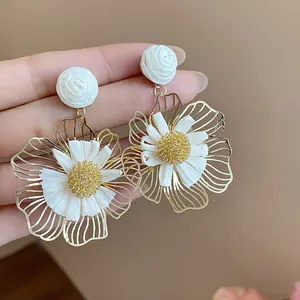 Detaillierte Makroansicht eleganter goldener Blumenohrringe mit weißen Raffia-Faserblättern.