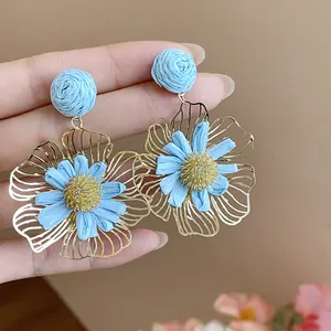 Detailaufnahme handgefertigter blauer Raffia-Blumenohrringe mit goldenen Blütenblättern.