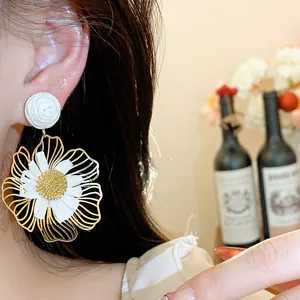 Nahaufnahme eines eleganten Gold- und weißen Raffia-Blumen-Ohrrings, getragen von einem Modell