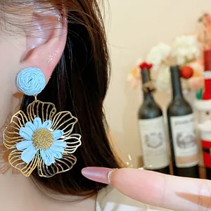 Detailansicht hellblauer Raffia-Blumenohrringe mit Goldkonturen am Ohr eines Models