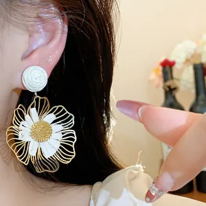 Detailaufnahme hochwertiger Ohrringe aus Goldmetall und weißem Bast in Blumenform