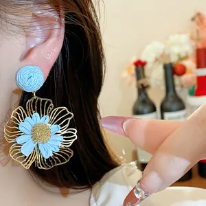 Detaillierte Nahaufnahme von blauem Bastblumen-Ohrring mit goldfarbenem Metallrahmen