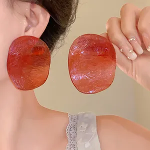 Close-up of large translucent reddish-orange acrylic disc earrings worn by an Asian model