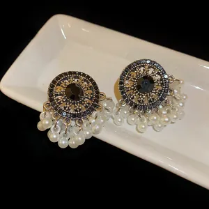 Detail of vintage earrings with black gemstone and white pearl tassels on a tray.