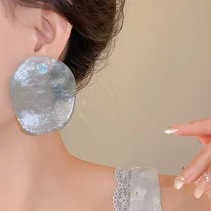 Detailed close-up shot of large textured silver disc earrings worn by a female model.