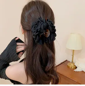 Macro detail of a stylish black fabric rose flower hair claw clip on long wavy brown hair.