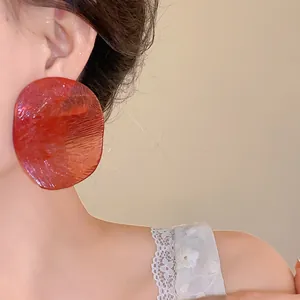 Close-up of oversized translucent red disc earrings worn by an Asian model