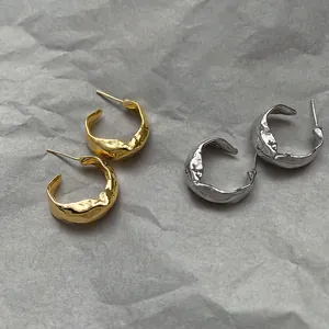 Detail of irregular gold and silver hoop earrings with a textured lava metal finish.