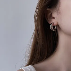Detailed close-up of an irregular silver textured hoop earring worn by a model