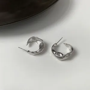 Close-up of minimalist irregular silver-plated hoop earrings with liquid metal texture.