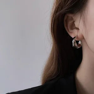 Side view detail of irregular silver-plated hoop earring worn on model's ear