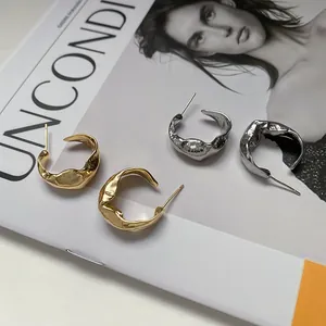 Detail view of irregular hammered hoop earrings in gold and silver finish on a magazine