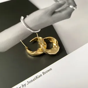 Close-up detail of irregular gold-plated hoop earrings on a magazine background