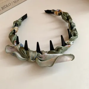 Detail view of a retro silk-wrapped headband featuring a soft bow and unique black spikes.