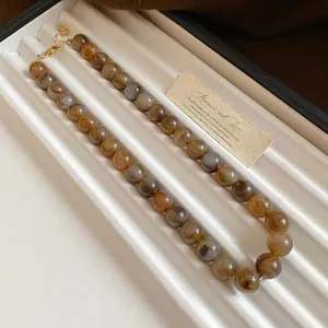 Détail du collier de perles marbrées avec des tourbillons ambre et gris élégant