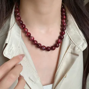 Gros plan d'un collier de perles marbrées rouge foncé porté sur une chemise en soie beige
