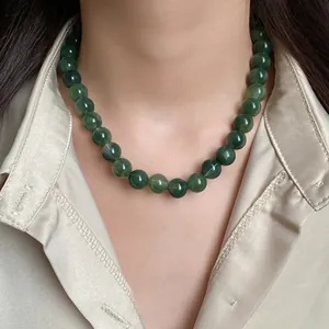 Gros plan d'un élégant collier de perles vertes porté avec une chemise en satin couleur champagne