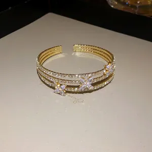 Vista dettagliata di un bracciale rigido dorato a tre strati con fiori in zircone lucenti.