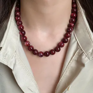 Détail d'un élégant collier de perles marbrées bordeaux porté par un mannequin