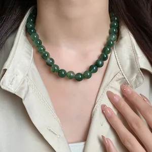 Vue détaillée d'un collier de perles vertes vintage porté avec une chemise en satin crème.
