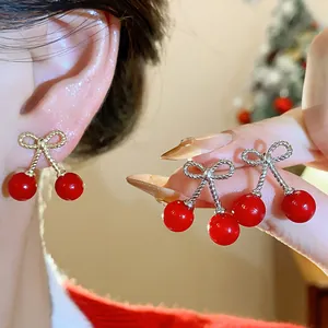 Close-up detail of stylish red cherry bow earrings worn on ear and held in hand for display