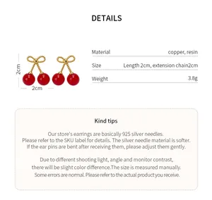 Close-up detail of red cherry drop earrings with gold bow and 925 silver needle specs.