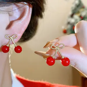 Detail of elegant red cherry earrings with golden bow designs shown on a model's ear.