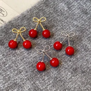 Close-up view of red cherry earrings with gold and silver bow-knot stems on gray wool fabric.