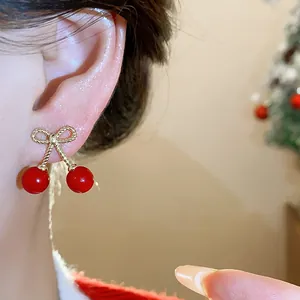 Detailed close-up of vibrant red cherry earrings with a gold bow on a person's ear