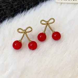 Close-up of red cherry earrings with gold bow detail on white faux fur background