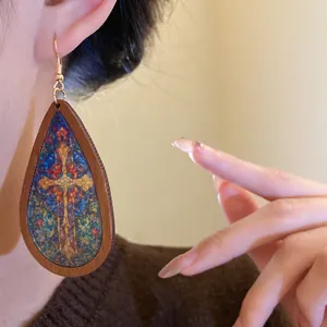 Close-up of wooden teardrop earring with colorful stained-glass cross pattern detail.