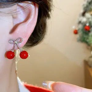 Close-up of elegant red cherry earrings with a silver bow detail worn on the ear.