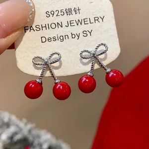 Detailed close-up view of cherry-shaped earrings featuring red beads and silver bow knots