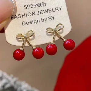 Detailed macro view of red cherry earrings with golden bow studs on S925 silver needles.