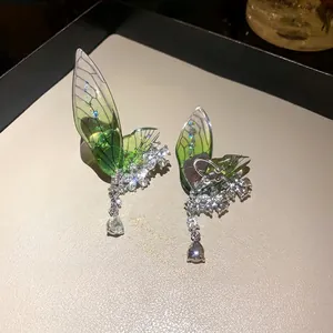 Elegant green wing ear cuffs with rhinestone flower details on a beige display tray.
