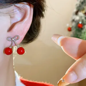 Macro view of dainty red cherry bow earrings worn on a female ear in a festive setting